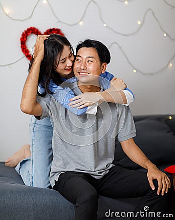 Asian young romantic lover couple female girlfriend hugging cuddling surprising male boyfriend celebration anniversary on cozy Stock Photo