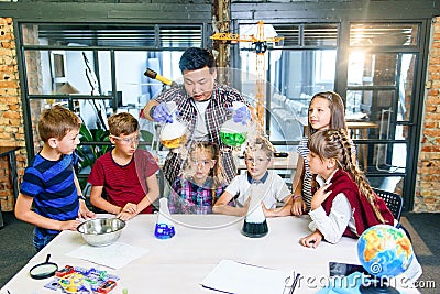 Asian young teacher with group of six cheerful caucasian 8-10 years pupils wearing protective glasses during chemical Stock Photo