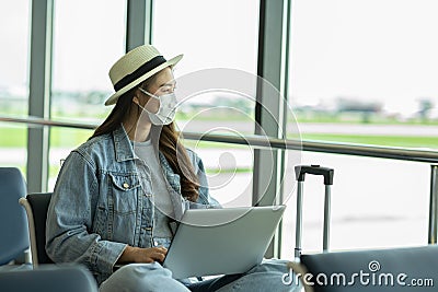 Asian young woman traveller wearing face maks using laptop computer at airport Due Covid-19 flu virus pandemic Stock Photo