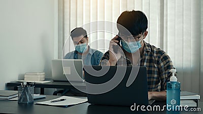 Asians sit in their office and use the phone to talk to clients while wearing masks in their offices during COVID-19 Stock Photo