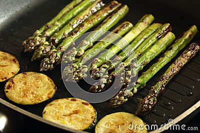 Asparagus and sliced courgette zucchini cooking in a griddle frying pan Stock Photo