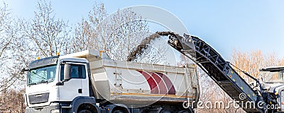 Asphalt milling and grinding machine at road repair and construction site throwing shredded old bitumen in big Editorial Stock Photo