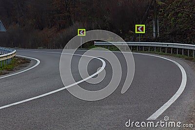 Asphalt road with bright traffic signs in situ of the sharp left turn Stock Photo