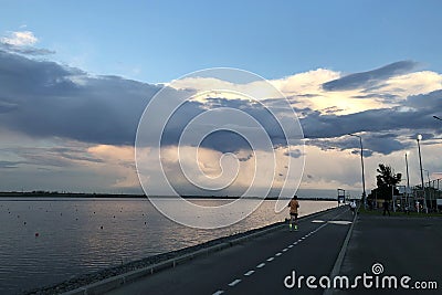 Asphalt road for jogging near lake, mans` silhouete running, Stock Photo