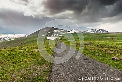 Road in rough terrain with snow-capped mountains and lush green meadows. The concept of travel in Iceland and the Nordic Stock Photo