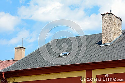 Asphalt shingles roof with skylights windows and rain gutter on the background of blue sky. House with old chimney. Stock Photo