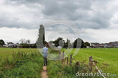 Asse, Flemish Brabant - Belgium - Man walking a soft trail between green agriculture fields Editorial Stock Photo