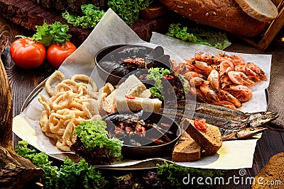 Assorted beer snacks: onion rings, smoked fish, mussels and shrimps on tray on sackcloth among vegetables Stock Photo