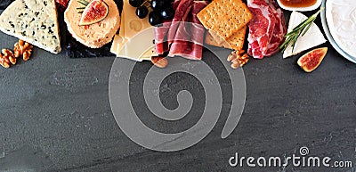 Assorted cheeses and meat appetizers, above view top border banner on a dark stone background with copy space Stock Photo