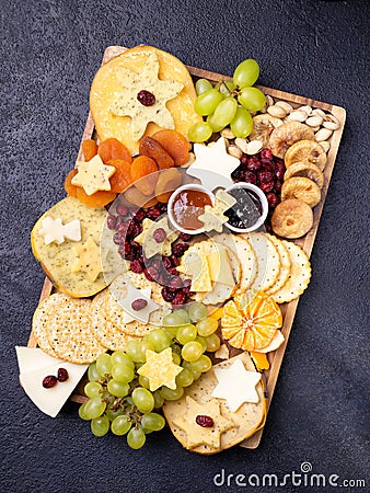 Assorted cheeses on wooden board plate hard cheese slices, walnuts, grapes, crackers, chutney mango, jam, dark background, top Stock Photo