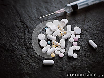 Assorted colorful pharmaceutical medicine pills tablets and capsules with hypodermic syringe injection needle on black stone Stock Photo