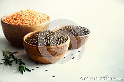 Assorted lentils. Marble, red and black raw organic lentils in wooden bowls with rosemary on grey concrete background Stock Photo