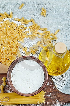 Assorted scattered uncooked pasta, a bottle of oil and a bowl of flour Stock Photo