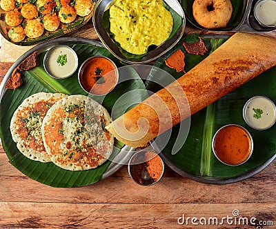 Assorted South indian breakfast foods on wooden background. Ghee dosa, uttappam,medhu vada,pongal,podi idly and chutney.. Dishes Stock Photo