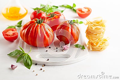 Assorted tomatoes with basil, garlic, spice and raw pasta for italian cuisine. Healthy food concept on white background Stock Photo