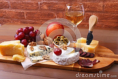 Assortment of cheese with fruits, grapes, nuts, glass with wine and cheese knife on a wooden serving tray Stock Photo
