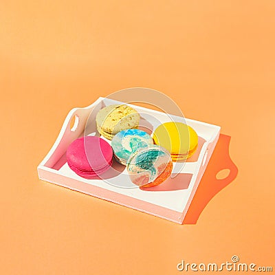 Assortment of colorful macaroons on wooden tray on orange background with sunlit. Dessert concept Stock Photo