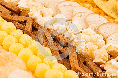 Assortment crunchy snacks - popcorn, nachos, croutons, corn sticks, potato chips as decorative stripes background, closeup. Stock Photo