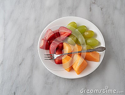 Assortment of fresh fruit with a fork on a white plate Stock Photo