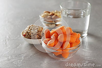 Assortment healthy snacks for dieting: baby carrots, nuts, granola bars and glass of water on table. Stock Photo
