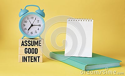 Assume good intentions. Inspirational quote with notepad to write on yellow background with alarm clock. Stock Photo