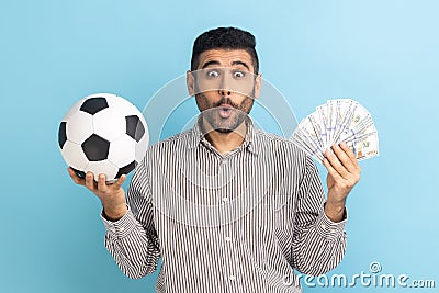 Astonished businessman holding soccer ball and fan of dollar bills, sports betting, big win. Stock Photo