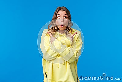 Astonished and excited young blond girl visit awesome place as cant decide what better buy, pointing fingers sideways at Stock Photo