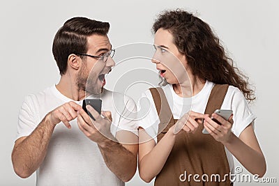 Astonished happy young couple holding mobile phones, pointing at screen. Stock Photo