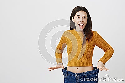 Astonished and happy young lady being impressed and excited because of losing weight, showing empty space in jeans by Stock Photo