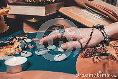 Astrology and esotericism. The female hand of the sorceress reads the runes. In the background, old books, fortune-telling runes, Stock Photo