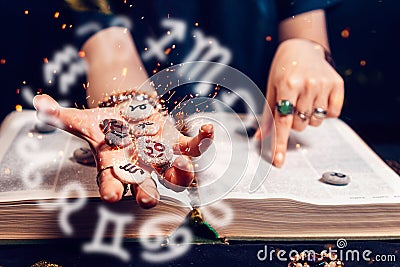 Astrology and horoscope. Fortune teller's hand holds the sparkling zodiac stones in the palm of her hand over the open Stock Photo