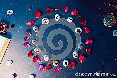 Astrology and horoscope. Stones with the signs of the zodiac, laid out in a circle, decorated with rose petals. Flat lay Stock Photo