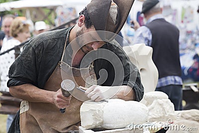 Asturias, Spain - 4 August 2019 : stone craftsman concentrated while sculpting a stone in a market in northern spain Editorial Stock Photo