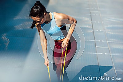 Athelte female working with elastic band outside on grey background. Healthy fit woman exercising with resistance band on a sunny Stock Photo