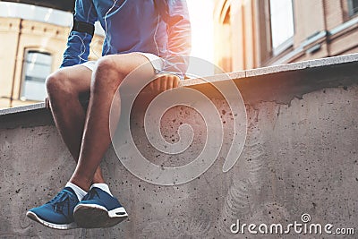 Athlete in blue running shoes sitting and resting after street workout session at sunset Stock Photo