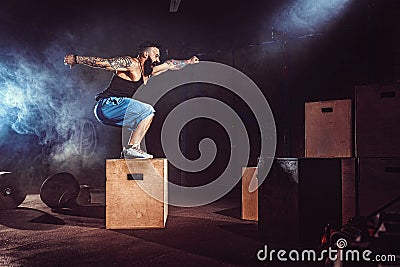 Athlete gave exercise. Jumping on the box. Phase touchdown. Gym shots in the dark tone. Smoke. Stock Photo