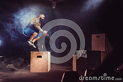 Athlete gave exercise. Jumping on the box. Phase touchdown. Gym shots in the dark tone. Smoke. Stock Photo