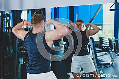 Athlete in the gym looks in the mirror at his muscles Stock Photo