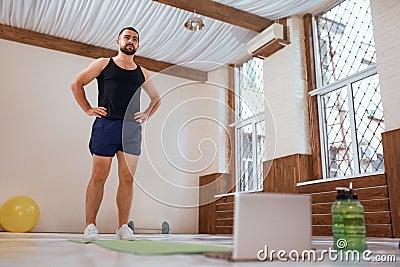 Athlete man trains hard in empty gym or home standing infront of laptop. Self isolated and motivated young man warm-up Stock Photo