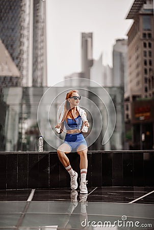 Athlete slim blonde fitness woman trainer runner in blue sportswear is sitting taking rest on form on city street Stock Photo
