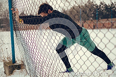 Athlete stretching calves on the fence on a snowy day Stock Photo