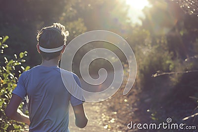 athlete in a sweatband jogging on a sunlit trail Stock Photo