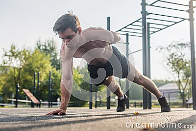 Athlete young man doing one-arm push-up exercise working out his upper body muscles outside in summer. Stock Photo