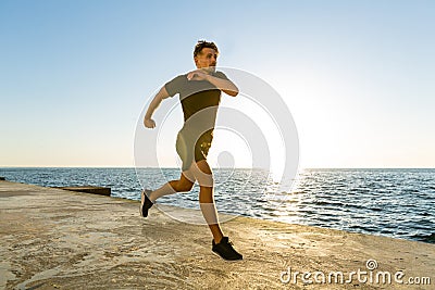 athletic adult man jogging on seashore in front Stock Photo