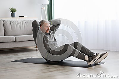 Athletic bearded senior man doing exercises for abs at home Stock Photo