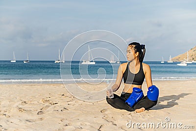Athletic beautiful Asian girl sitting on the sand after a boxing workout and drinks water Stock Photo
