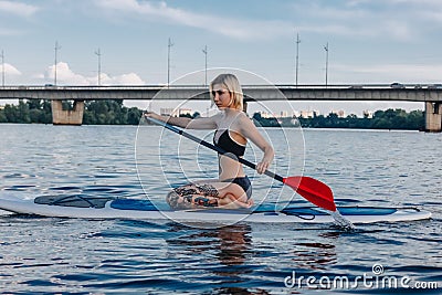 athletic blonde girl sitting on sup board Stock Photo