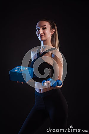 Athletic blonde holding dumbbells and gift box in her hands Stock Photo
