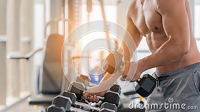 Athletic bodybuilder man lifting dumbbell from rack in gym and fitness club Stock Photo