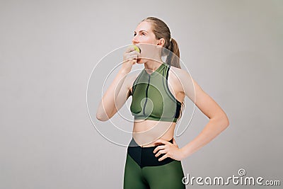 Athletic girl bites green apple. Fitness bikini athlete eats before training. Model is starving Stock Photo